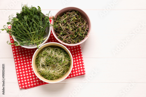 Different types of microgreens on white tiled table, flat lay. Space for text