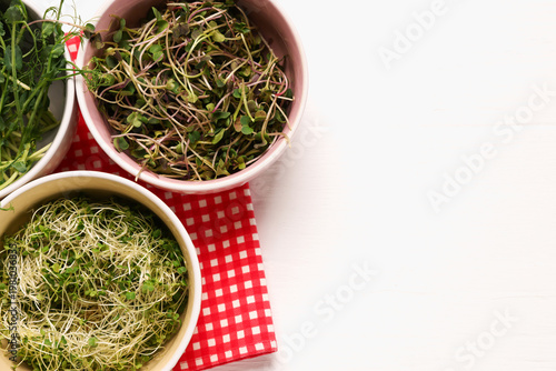 Different types of microgreens on white tiled table, flat lay. Space for text