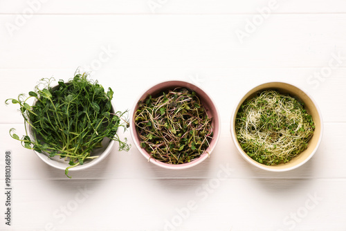 Different types of microgreens on white tiled table, flat lay