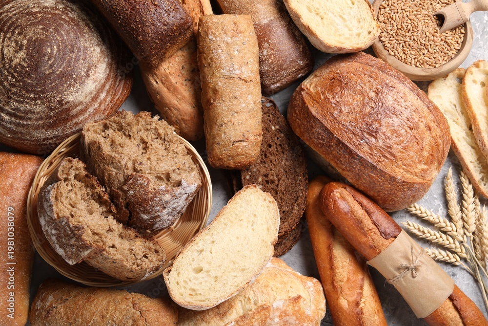 Obraz premium Different types of bread, grains and spikes on grey table, flat lay
