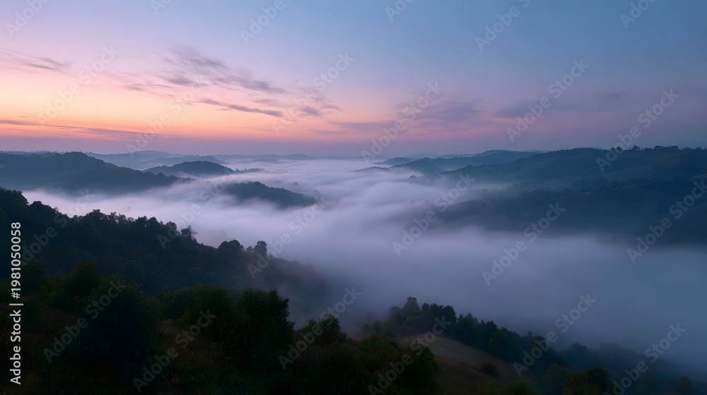 Obraz premium Rolling layered hills emerging from dense morning mist beneath a vibrant pastel dawn sky