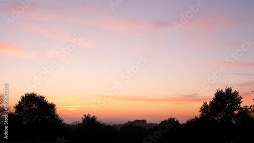 Peaceful dawn landscape with colorful clouds and tree silhouettes