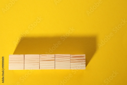 Blank wooden cubes on yellow background, flat lay. Space for text