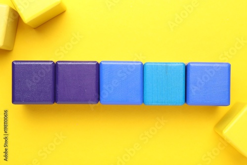 Empty colorful wooden cubes on yellow background, flat lay. Space for text