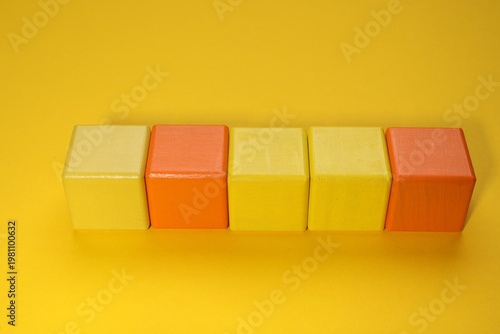 Empty colorful wooden cubes on yellow background, above view. Space for text