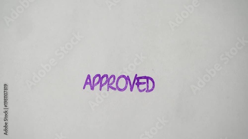 Rubber stamp prints approved text in purple ink over empty white sheet during review completion.
