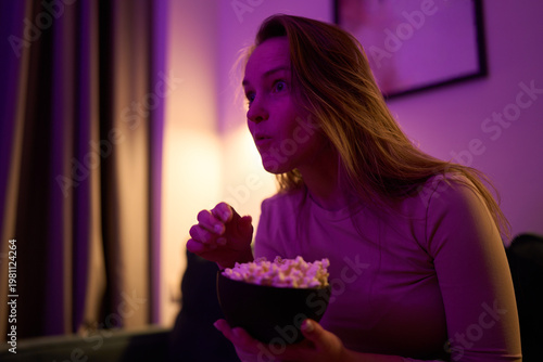 Female sitting with popcorn reacting to screen in dim living room