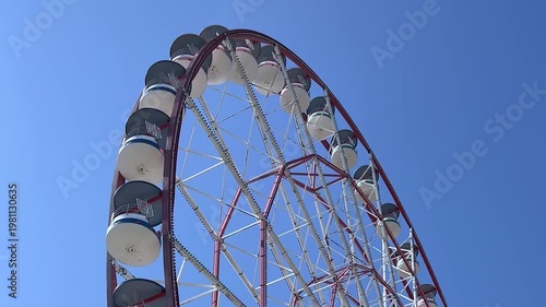 Horizontal video. Bottom view. Blue ferris wheel cabin spins against blue sky. Concept of carousel, holiday, transport, tourism, travel, entertainment in resort city, rides, vacation, recreation, fair