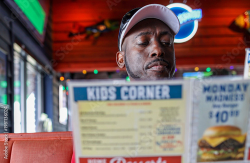 A portrait of a black man reading a menu at a restaurant