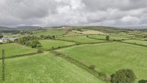 Wallpaper Mural Expansive rural landscape with bright green fields separated by dense hedgerows and scattered trees under an overcast sky. A farm complex sits among the distant hills. Torontodigital.ca