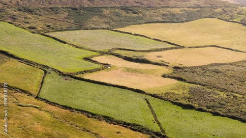 An aerial view captures a diverse rural landscape showcasing small, irregularly shaped fields in varying shades of green and golden brown, typical of the Irish countryside in late summer.