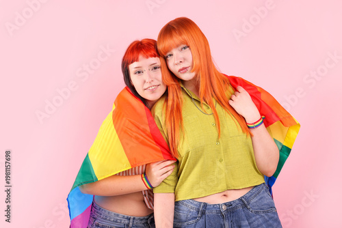 Lovely lesbian couple with rainbow flag on pink background. LGBT concept
