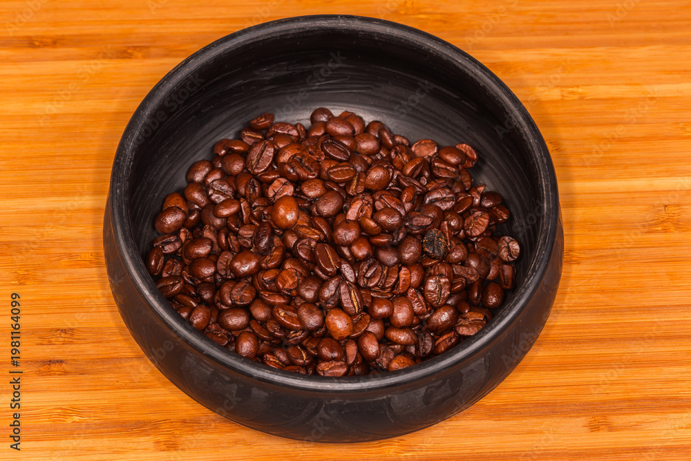 Fototapeta premium Roasted coffee beans in black clay bowl on wooden surface