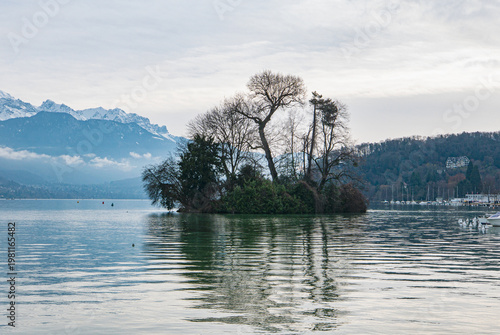 landscape of Lac d´Annecy in France with mountains in background and an island with trees in the middle and boats at shore