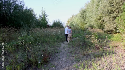 A couple slowly walks along a narrow path through tall grass during a long countryside walk