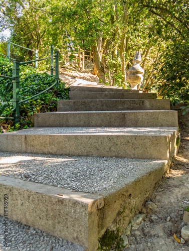 Visitors walk up the steps in Este Castle park in Padua, Italy, on a sunny day surrounded by trees and greenery