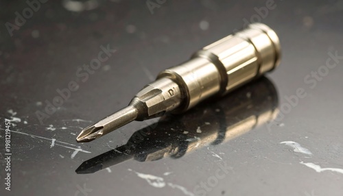 Silver screwdriver bit with precision tip, lies on a dark, reflective marble surface