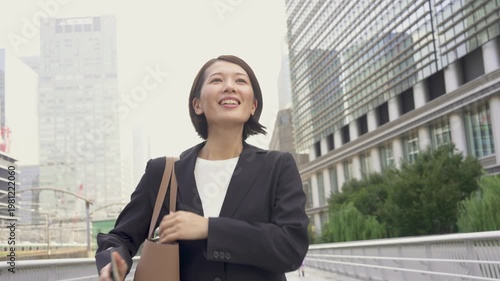 Japanese Businesswoman Commuting Outdoors with Smartphone, Confident Smile, Urban Business District, Sales and Work