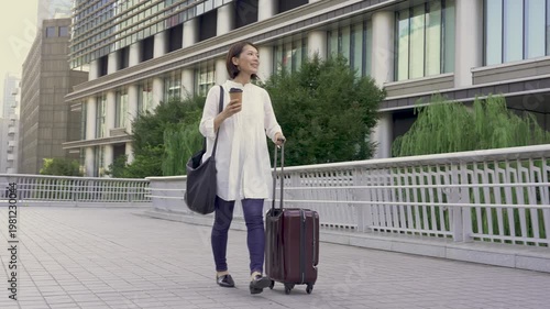 Japanese Woman Walking with Suitcase and Coffee, Casual Travel, Smiling Outdoors, Urban Street