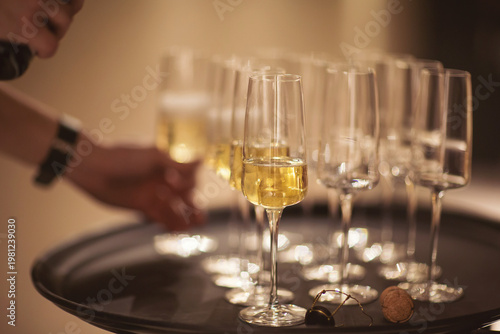 A person carefully balances a tray filled with fine crystal glasses containing golden bubbly. The setting suggests a festive occasion, inviting joy and togetherness