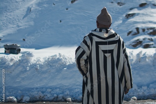 Man in striped djellaba facing snow in Atlas Mountains