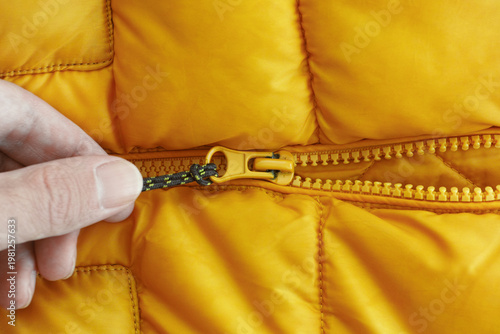 A hand pulling the zipper of a bright orange puffer jacket. Close up.