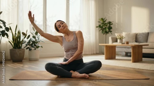 Athletic Young Woman Sitting On A Yoga Mat In A Bright Modern Living Room. Seated Yoga Preparation, Natural Daylight, And A Clean Home Interior Shape The Stretch Setup