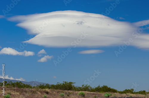 Windy Mojave Desert landscape with a prominent lenticular cloud and bright blue skies in California.