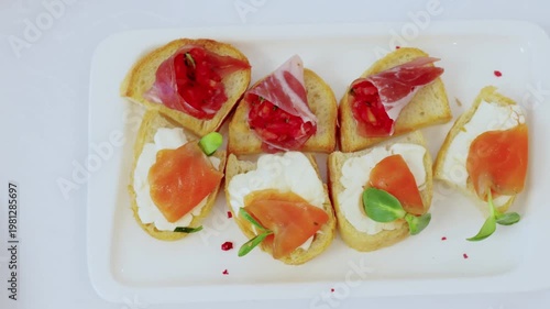 Elegant appetizers combining crispy toasted bread, creamy cheese, smoked salmon, prosciutto, garnished with fresh microgreens on pristine plate