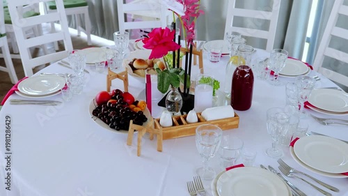 Elegant dining setup with white linen, pink rose centerpiece, wooden fruit display, fine tableware creating sophisticated table arrangement