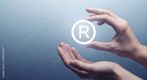 Hands holding a white registered trademark symbol on a soft blue background. Symbolizing corporate branding, legal security, patent ownership, and intellectual property protection strategies