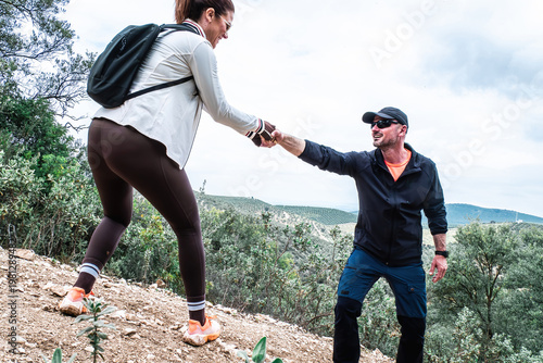 Two hikers demonstrating teamwork and assistance on a challenging mountain path, showing support and cooperation outdoors