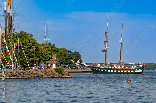 Tall Ship under engine power moving into harbor with anchored other tall ships.