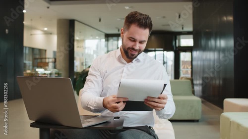 Caucasian businessman accountant working with financial graph documents, calculate taxes for charts and reports in modern office lobby. Smiling male manager working on laptop, planning expenses budget