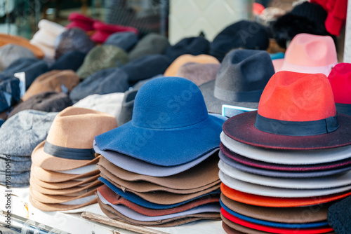 Fashion Stylist Picks Colorful Layered Hats Amidst Lively Outdoor Marketplace Setting