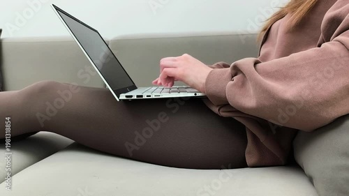 Closeup hands type quickly on laptop keyboard while sitting on sofa. Female performs online work entering text in indoor environment.