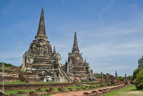 Fotografie Three ancient chedis of Wat Phra Si Sanphet rising behind a red brick wall in golden light at Ayutthaya Historical Park, Thailand
