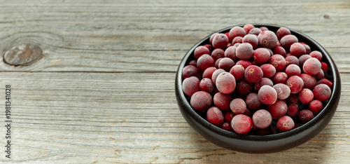 Raw, frozen cranberries in a bowl. Rustic wooden background with space for additional content. 