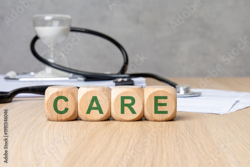 CARE word in green on wooden blocks. Blurred medical background with stethoscope, hourglass and documents. Healthcare concept.