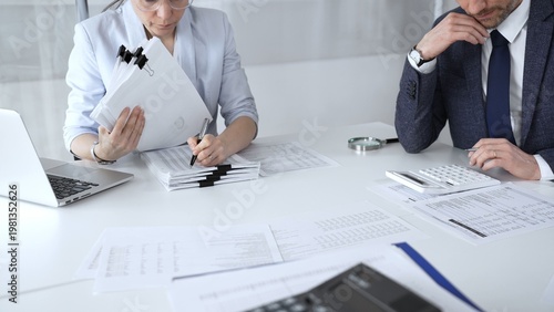 Tableau sur toile Professional auditors reviewing financial paperwork, using magnifying glass and calculator while analyzing business documents for detailed inspection and accounting compliance
