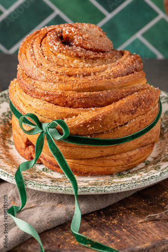 Wallpaper Mural A vertical shot of a beautifully layered puff pastry Easter bread coated in cinnamon sugar and tied with a green velvet bow on a vintage floral plate Torontodigital.ca
