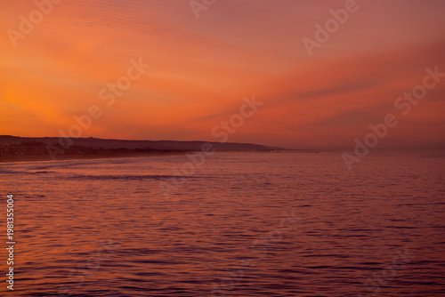 Tablou pe pânză Vibrant fiery orange sunrise over the Pacific Ocean coast with purple water refl