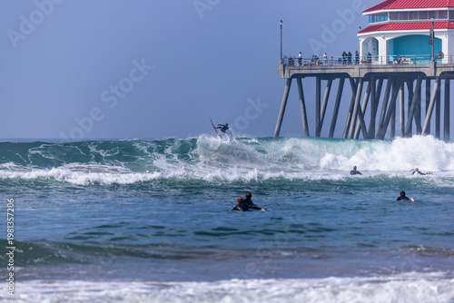 Фотография Surfer performing an aerial maneuver on a wave next to the Huntington Beach Pier