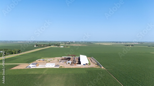 Farmland landscape featuring a large agricultural facility under a clear blue sky in the Midwest during summer