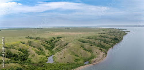 Expansive green hills and calm waters along the river under a cloudy sky near the countryside