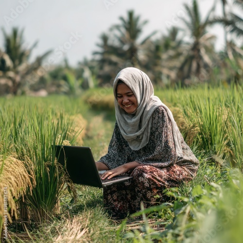 Happy Young Woman Wearing Headscarf Using Laptop in Green Rice Field