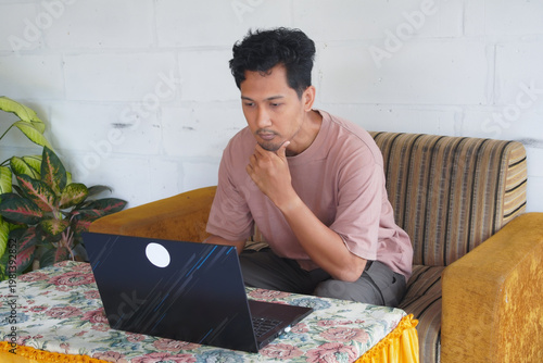 Young man concentrating on laptop, making decisions, or solving problems, capturing the essence of remote work and digital innovation in a contemporary home setting