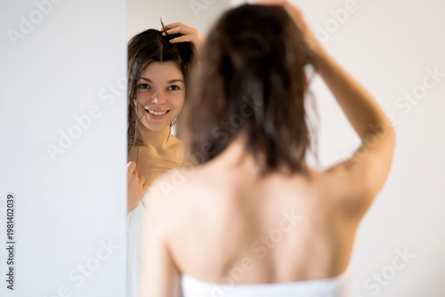 A girl in a white towel looks in the mirror and takes care of her beauty.