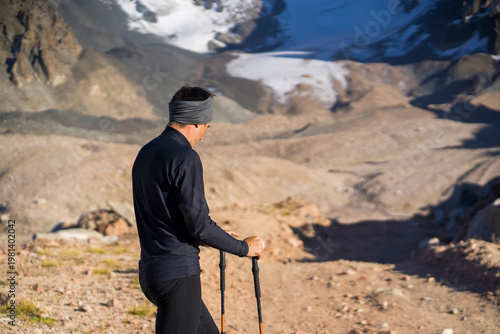 Traveler with trekking poles is walking in the snowy mountains.