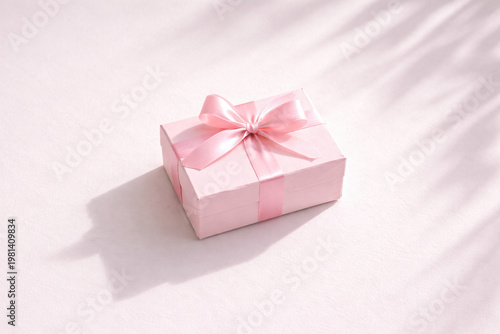 Minimalist composition with a single pink gift box and ribbon on clean white background, strong natural light casting elegant shadow, modern and premium aesthetic with copy space.